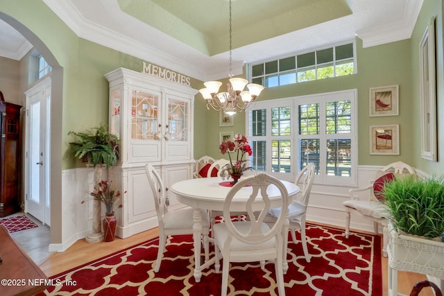 dining space with a tray ceiling, crown molding, arched walkways, and light wood finished floors