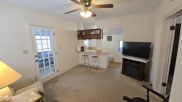 living area featuring a ceiling fan, baseboards, and light carpet