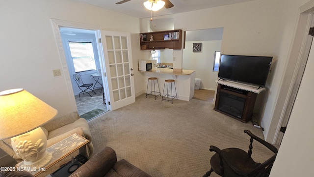 living room featuring a ceiling fan, baseboards, a fireplace, french doors, and light carpet