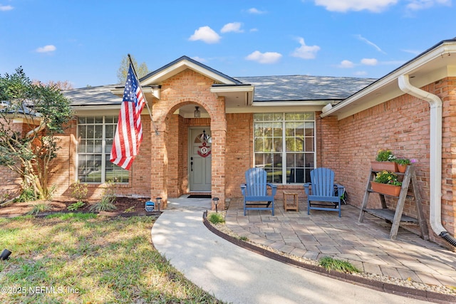 doorway to property with brick siding, a shingled roof, and a patio area