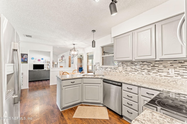 kitchen featuring dark wood finished floors, a peninsula, a sink, appliances with stainless steel finishes, and tasteful backsplash