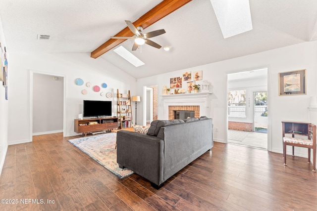 living area featuring a ceiling fan, dark wood-style floors, visible vents, lofted ceiling with skylight, and a brick fireplace