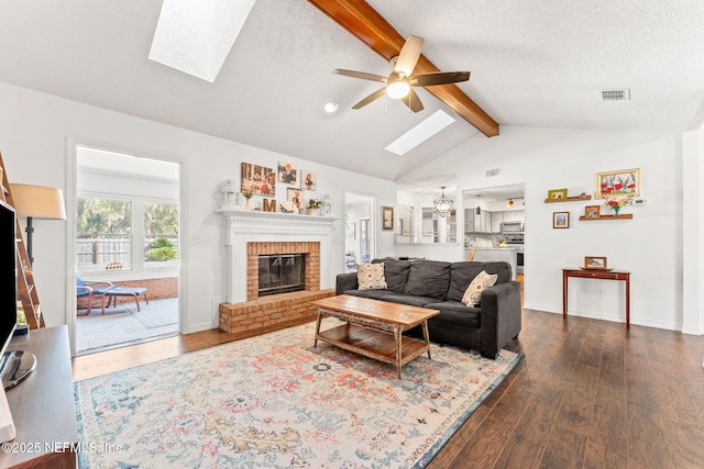 living area featuring dark wood-style floors, visible vents, lofted ceiling with skylight, and a brick fireplace