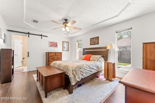 bedroom with visible vents, multiple windows, a barn door, and wood finished floors