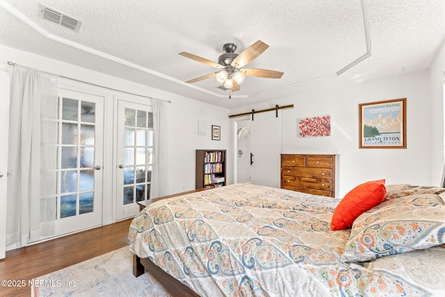 bedroom with a ceiling fan, wood finished floors, visible vents, a textured ceiling, and a barn door