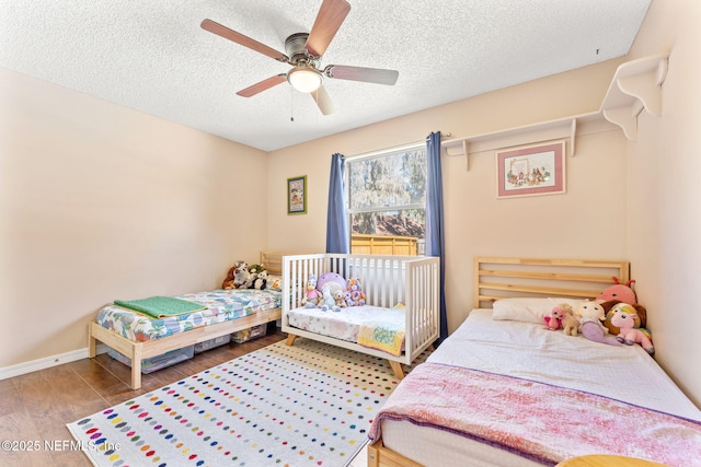 bedroom with ceiling fan, baseboards, a textured ceiling, and wood finished floors