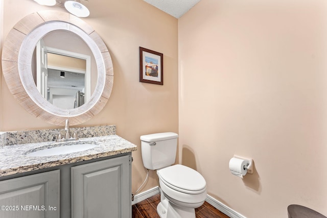 half bathroom featuring toilet, vanity, baseboards, and wood finished floors