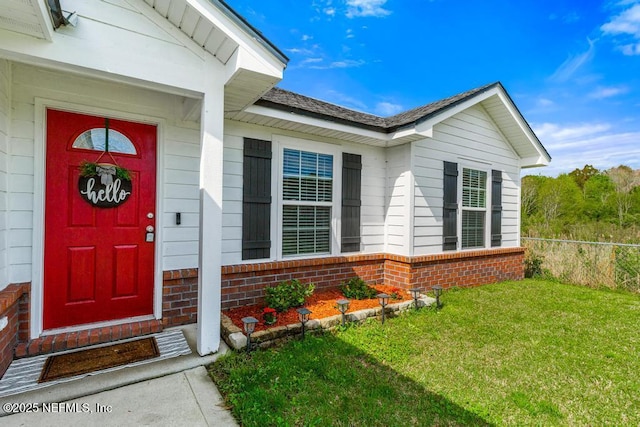 entrance to property featuring brick siding, fence, and a lawn