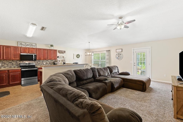 living area with baseboards, a ceiling fan, visible vents, and a textured ceiling