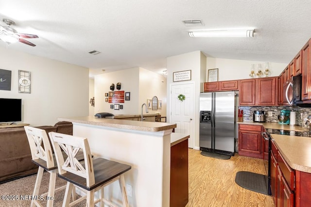 kitchen featuring visible vents, ceiling fan, a kitchen breakfast bar, stainless steel appliances, and reddish brown cabinets