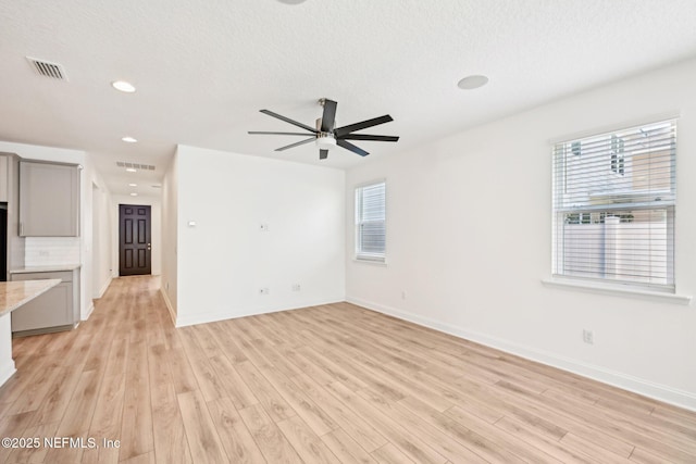 unfurnished living room featuring a wealth of natural light, visible vents, and light wood-style floors