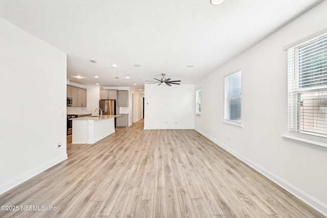 unfurnished living room with a sink, baseboards, recessed lighting, and light wood finished floors