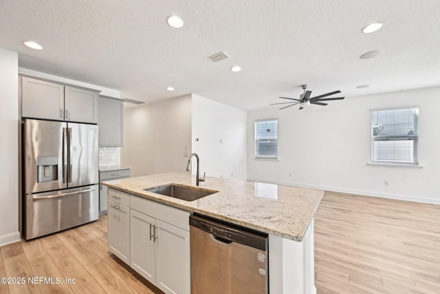 kitchen with visible vents, light wood-type flooring, light stone counters, appliances with stainless steel finishes, and a sink