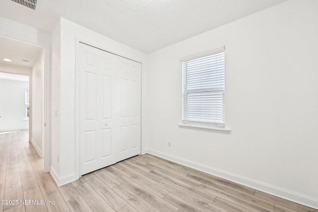 unfurnished bedroom with a closet, visible vents, multiple windows, and light wood-type flooring