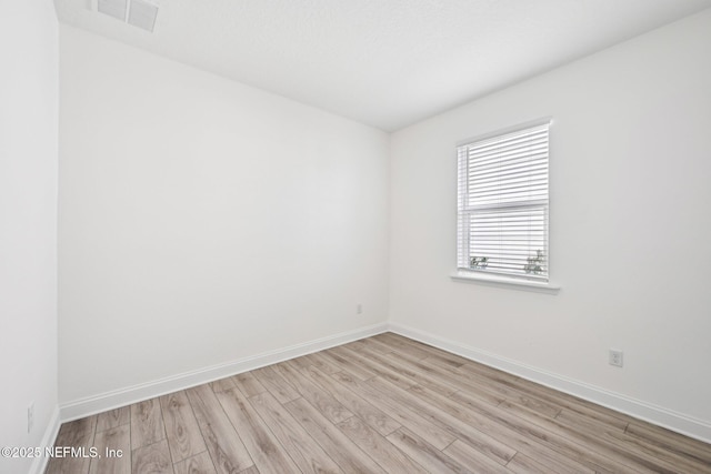 unfurnished room featuring light wood finished floors, visible vents, and baseboards