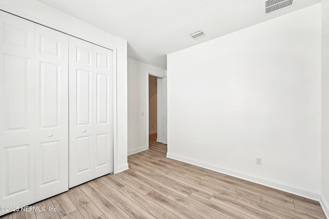 unfurnished bedroom with visible vents, baseboards, a closet, and light wood finished floors