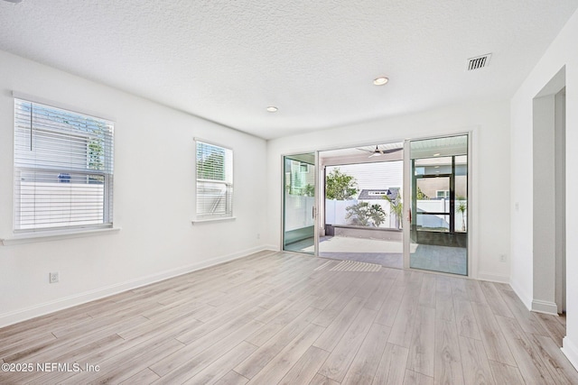 spare room featuring baseboards, visible vents, light wood finished floors, recessed lighting, and a textured ceiling