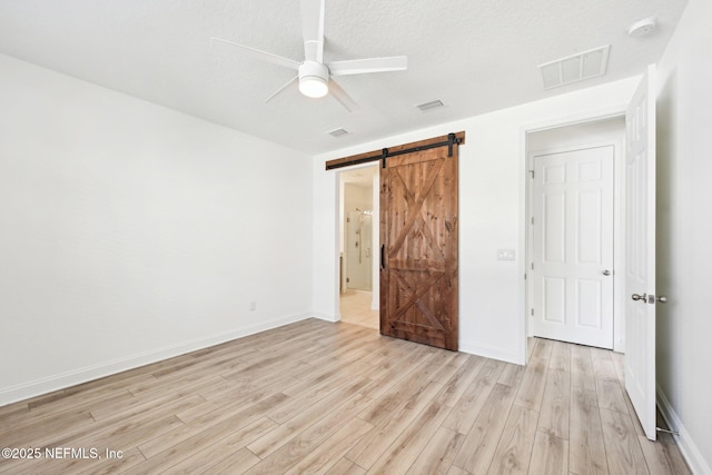 unfurnished bedroom with visible vents, a ceiling fan, a barn door, light wood-style floors, and baseboards