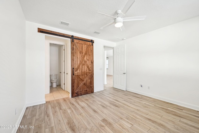 unfurnished bedroom featuring light wood-type flooring, visible vents, a barn door, and baseboards