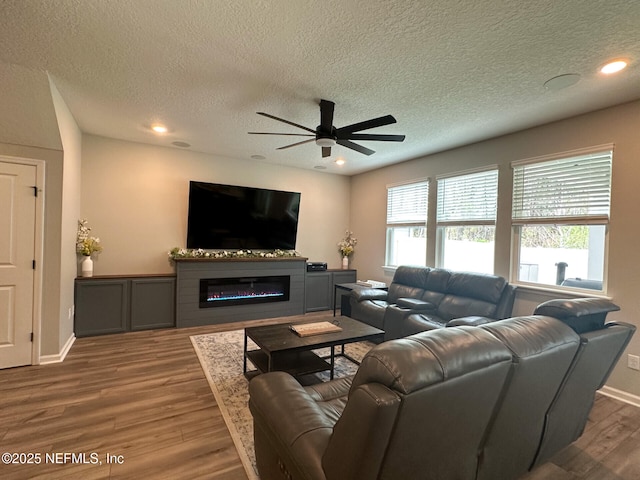 living area with plenty of natural light, ceiling fan, a glass covered fireplace, and wood finished floors