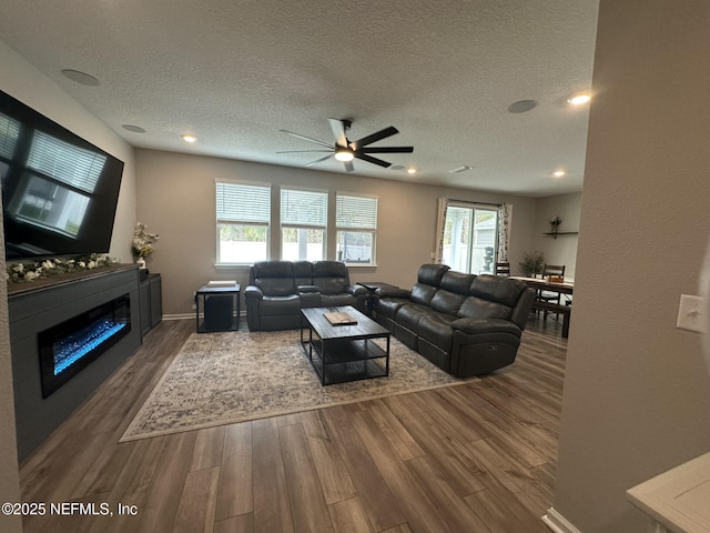 living area with a glass covered fireplace, ceiling fan, wood finished floors, and a textured ceiling