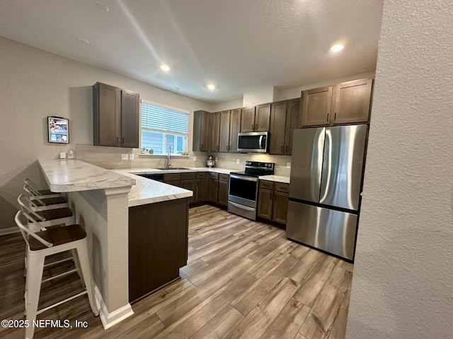 kitchen with light wood finished floors, a breakfast bar, a peninsula, stainless steel appliances, and a sink