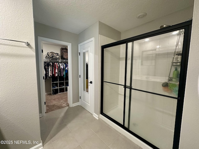 bathroom with a textured ceiling, a shower stall, tile patterned flooring, baseboards, and a spacious closet