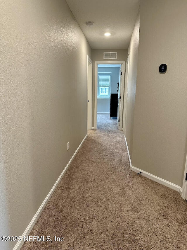 hallway with visible vents, carpet flooring, baseboards, and a textured wall