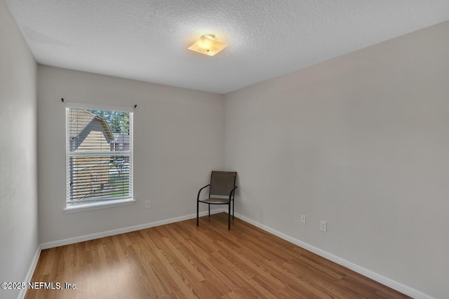 spare room featuring wood finished floors, baseboards, and a textured ceiling