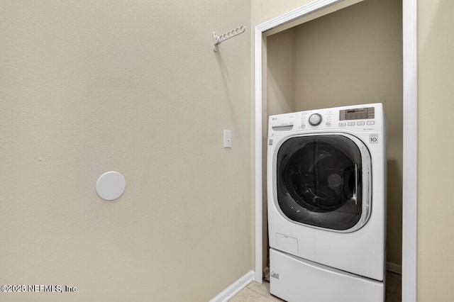 clothes washing area featuring light tile patterned floors, baseboards, washer / clothes dryer, and laundry area