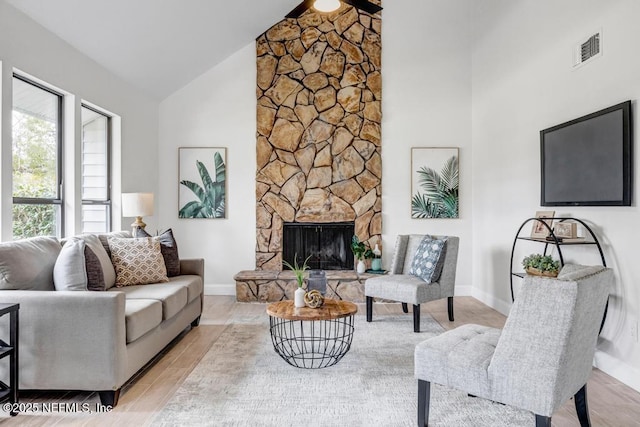 living area featuring visible vents, baseboards, high vaulted ceiling, and a stone fireplace