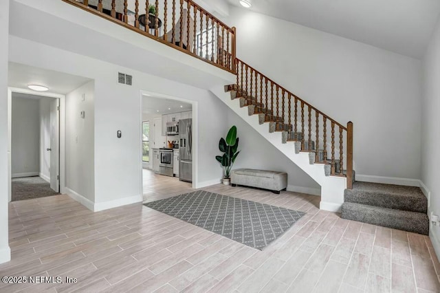 entrance foyer featuring visible vents, baseboards, wood finish floors, stairs, and a towering ceiling