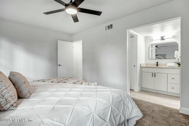 bedroom with a ceiling fan, visible vents, a sink, ensuite bathroom, and light colored carpet