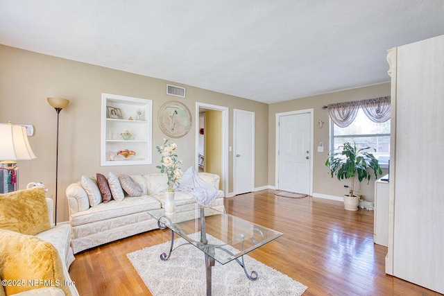 living area featuring visible vents, built in shelves, baseboards, and wood finished floors