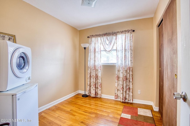 laundry area with laundry area, wood finished floors, baseboards, and stacked washing maching and dryer