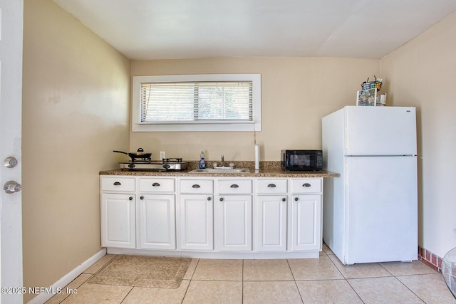 kitchen featuring a sink, freestanding refrigerator, white cabinets, black microwave, and light tile patterned floors