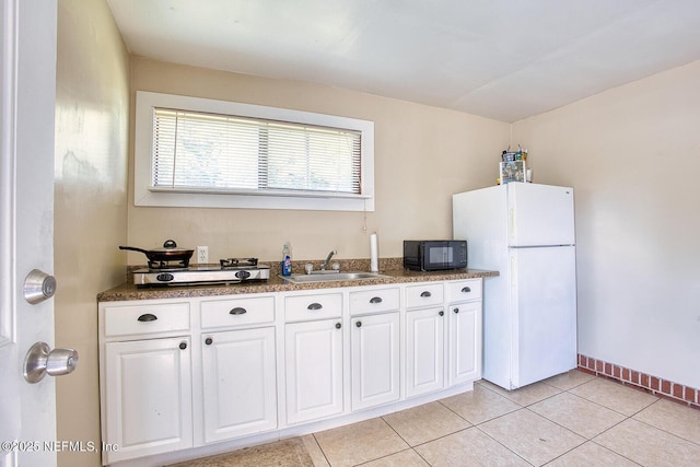 kitchen featuring light tile patterned floors, freestanding refrigerator, a sink, white cabinets, and black microwave