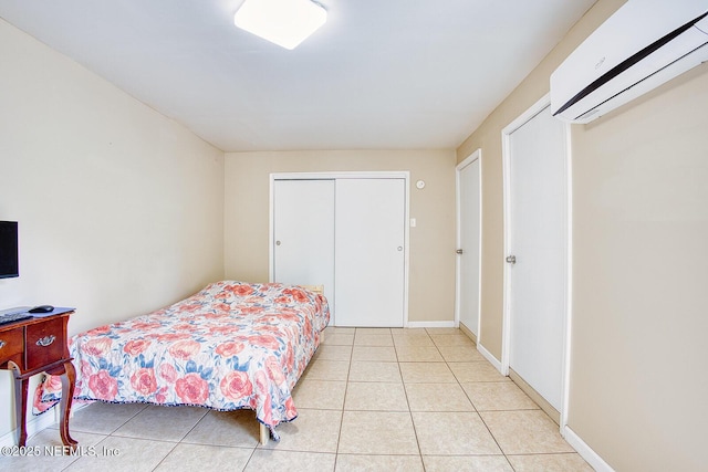 bedroom featuring light tile patterned floors, a closet, baseboards, and an AC wall unit