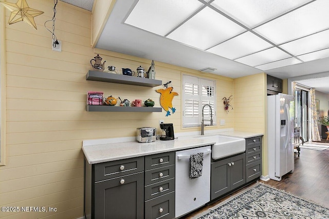 kitchen with a sink, light stone counters, stainless steel dishwasher, white fridge with ice dispenser, and dark wood-style flooring