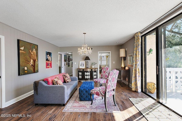 living area featuring a notable chandelier, a textured ceiling, baseboards, and wood finished floors