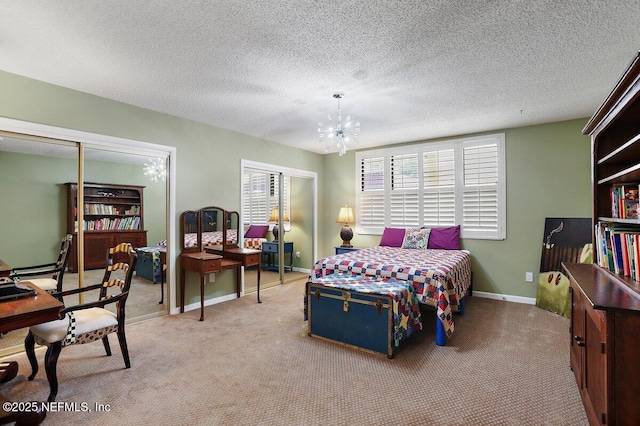 carpeted bedroom featuring a notable chandelier, a textured ceiling, baseboards, and multiple closets