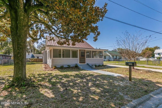 view of front facade with metal roof, fence, a front yard, and a sunroom