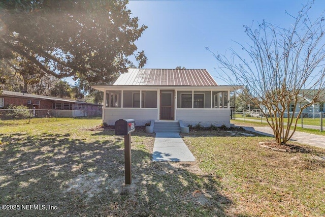 view of front of property featuring metal roof, fence, a front yard, and a sunroom