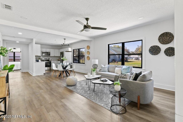 living area featuring visible vents, a textured ceiling, light wood-type flooring, and baseboards