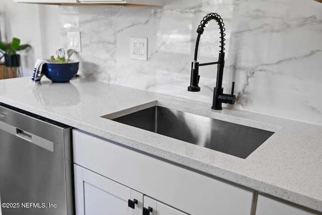 kitchen with a sink, stainless steel dishwasher, white cabinets, decorative backsplash, and light stone countertops