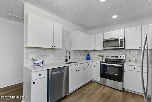 kitchen with dark wood finished floors, appliances with stainless steel finishes, white cabinetry, and a sink