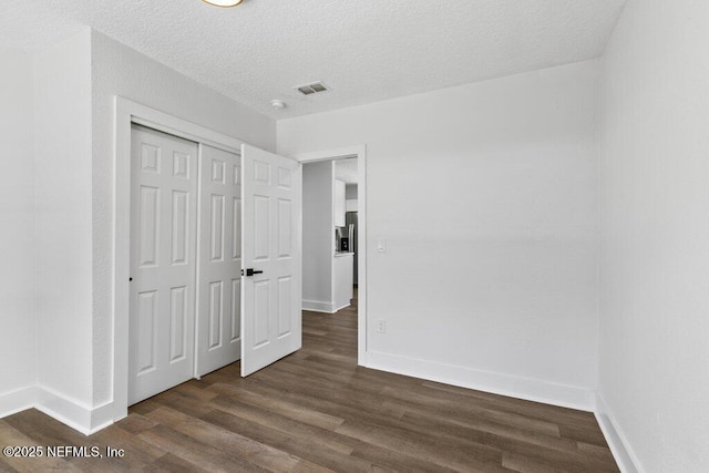 unfurnished bedroom with visible vents, baseboards, dark wood finished floors, a closet, and a textured ceiling