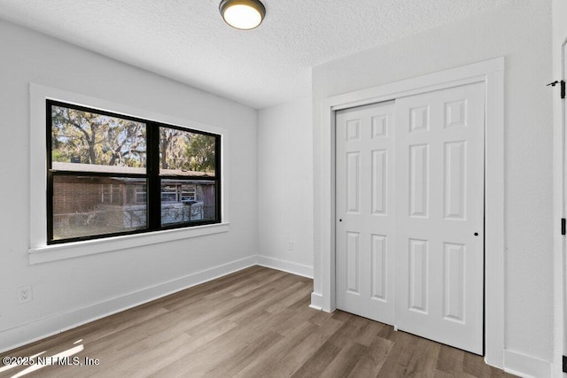 unfurnished bedroom featuring baseboards, wood finished floors, a closet, and a textured ceiling