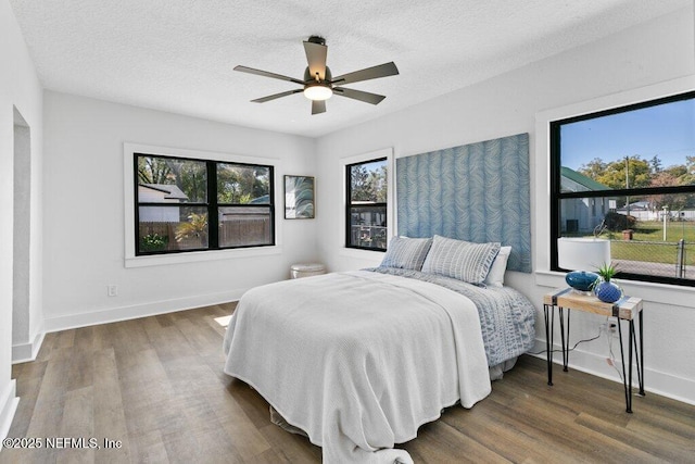 bedroom with a textured ceiling, a ceiling fan, baseboards, and wood finished floors