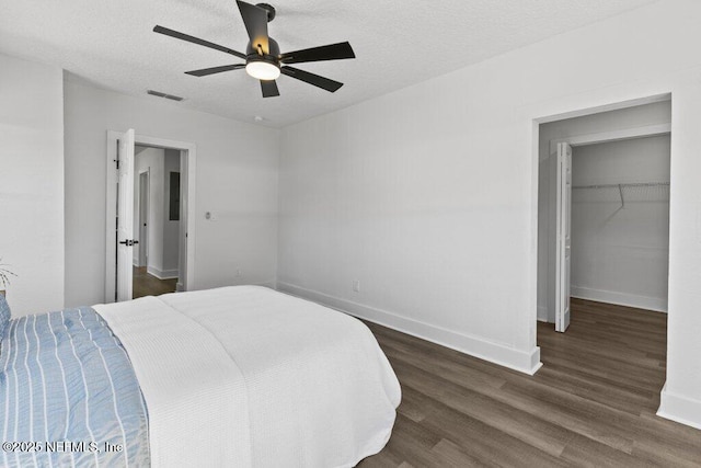 bedroom with a walk in closet, visible vents, a textured ceiling, wood finished floors, and baseboards